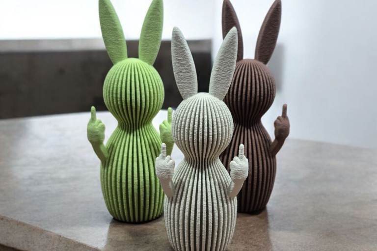 Weihnachtsmänner 3D-Druck Drei dekorative Weihnachtsfiguren aus 3D-Druck in Rosa, Khaki und Schwarz zwischen kleinen Tannenbäumen.